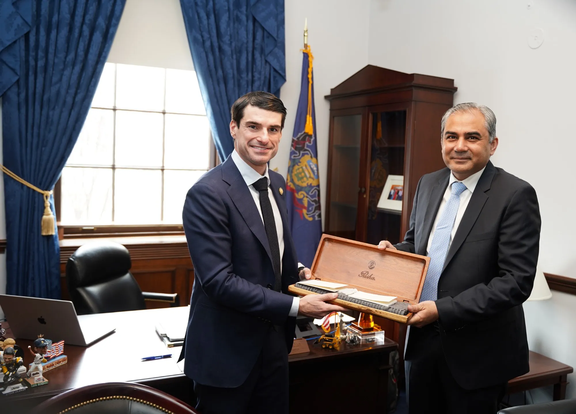 Two men in suits hold an open wooden gift box together during an official office meeting